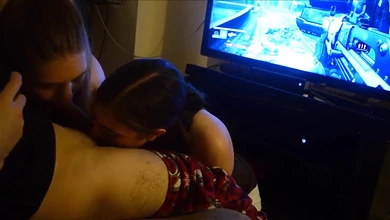 Пока парень играет в приставку, его тёлка с подружкой сочно насасывают ему хуй